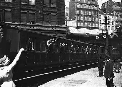 Voitures pleines de soldats s'éloignant du quai de la gare.
