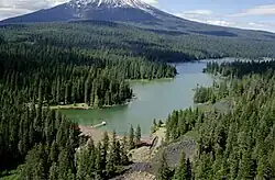 Du terrain boisé avec un lac dans l'avant-plan et une montagne couverte de neige dans l'arrière-plan