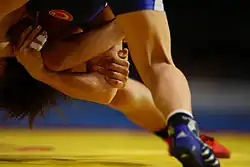 Photo en couleur d'un match de lutte en cours, ne montrant que les jambes et mains des lutteuses.