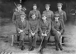 Photographie noir et blanc d'un groupe de 8 hommes en uniforme, formant deux rangs de 4. Le premier rang est assis tandis que le deuxième, derrière, est debout.
