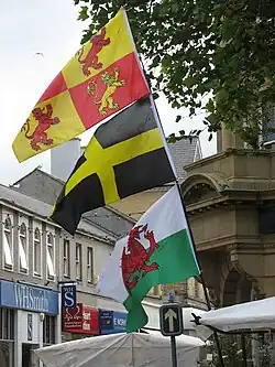 Photo montrant trois drapeaux accrochés à la même hampe dans un décor urbain