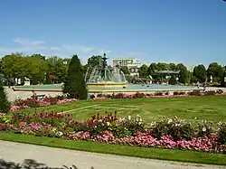  Photographie d'un jardin public, ses massifs de fleur et sa grande fontaine.