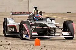 Photographie d'une monoplace de Formule E grise, noire et rouge, vue de face, dans son ensemble.