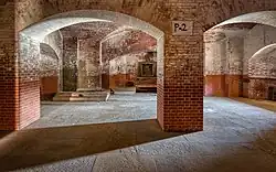 Cave légèrement voûtée, sol qui semble cimenté, murs qui semblent en briques, le bas rouge et le reste blanchâtre.