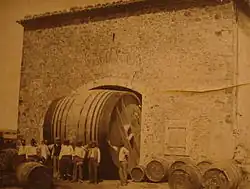 La photographie en noir et blanc jaunie par le temps indique une image issue de la fin du XIXe&nbsp;siècle ou du début du XXe&nbsp;siècle. Elle montre des barriques entreposées dans la cour d'un chai et huit ouvriers qui posent devant un foudre qui passe juste sous la voute du portail d'entrée de la cave.