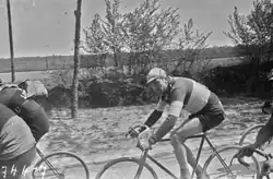 Photographie en noir et blanc montrant un cycliste en course au sein du peloton.