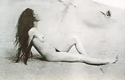 Louise Bryan de profil, nue sur une plage, se chauffant au soleil, cheveux longs non coiffés
