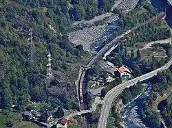 Vue aérienne d’une voie de chemin de fer en courbe, proche d’une route, en fond de vallée.