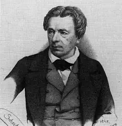 Noir et blanc, en costume 3 pièces, chemise à col cassé blanche et gilet gris avec veste anthracite à larges revers, avec nœuds papillon noir. Visage en triangle bas, cheveux blonds ou châtains clairs, yeux clairs, nez assez fort et droit
