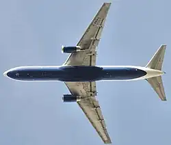 Vue de dessous d'un avion à réaction en vol. Un moteur est accroché à chacune des deux ailes. L’empennage horizontal est à l'arrière.