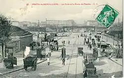 La porte de la Villette avant 1910 : au premier plan la percée dans le mur d'enceinte, par lequel passe la RN2, alors appelée « route de Flandre », et ses voies de tramways et le pont de la ligne Pantin - La Plaine.