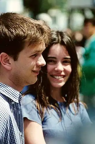 Une jeune fille brune souriante, cheveux longs et yeux sombres, de face, et un jeune homme de profil