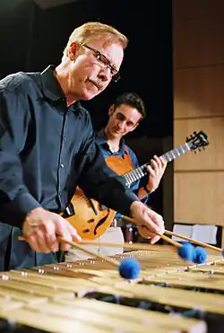 un homme moustachu au vibraphone, un guitariste en arrière-plan