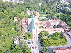Photographie aérienne d'un monastère flanqué sur sa gauche d'une église dont la façade est encadrée de deux flèches