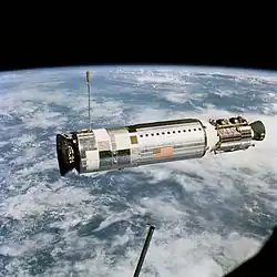 Photographie en couleur d'un véhicule spatiale cylindrique en orbite autour de la Terre.