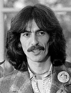 Photographie en noir et blanc d'un homme aux cheveux longs bruns portant la moustache, regardant vers sa gauche.