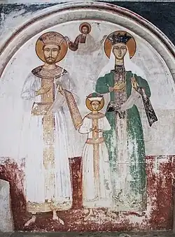 Dessin en noir et blanc sur un mur montrant un couple avec un enfant, au-dessus d'eux un homme est dessiné