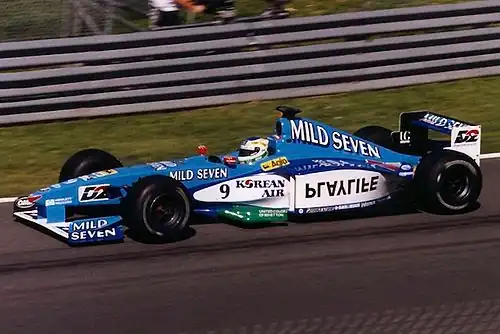 Photographie en couleur d'une Formule 1 bleu ciel et blanche, dans son ensemble, de profil gauche, sur de l'asphalte.