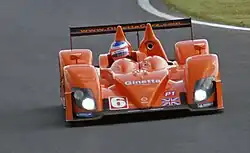 Phographie d'une voiture orange, vue de face, sur une piste.