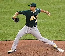 Un joueur de baseball habillé d'un T-shirt vert foncé et d'un pantalon gris en train de lancer une balle.