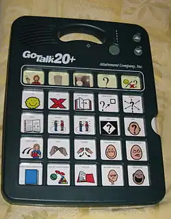 Système électronique de communication vocale avec haut-parleurs, comportant une fente pour insérer différentes cartes. Ici, la carte comporte 25 symboles issus d'un livret de lecture.