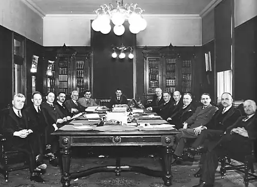 Photographie noir et blanc de quatorze hommes assis autour d'une table.
