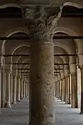 Une colonne à fût en marbre veiné et à chapiteau corinthien à l'intérieur du portique occidental. En arrière-plan, l'alignement symétrique des arcades.