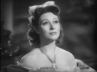 Photo en noir et blanc. L'actrice, en robe de bal très décolletée, lève la tête