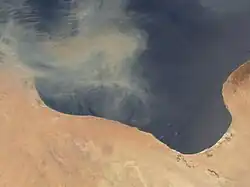 Photo satellite avec une partie de désert au sud et une partie de mer au nord. Le trait de côte, situé au milieu, est irrégulier et forme un renfoncement sur les terres.