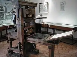 Une machine à imprimer en bois, au milieu d'une salle d'exposition avec des visiteurs.