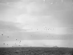 Photo en noir et blanc de deux navires entourés de fumées attaqués par des avions.