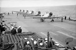 Photo en noir et blanc d'avions alignés sur le pont d'un porte-avions.