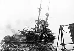 Photographie d'un navire donnant de la bande sur tribord dont la tourelle arrière est complètement déchiquetée