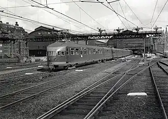 Départ d'un long train d'Amsterdam-Central comportant une rame quadruple et une remorque postale.