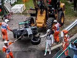 Photographie d'un engin de levage transportant une monoplace de Formule 1 endommagée