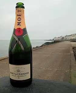 Bouteille verte ouverte en premier plan, sur une esplanade où l'on voit la mer en arrière-plan.