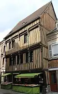 Maison du XVe siècle entièrement en pans de bois, façade à encorbellements et son étal de fruits et légumes.