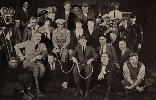 Photographie en noir et blanc de l'équipe du film rassemblée pour l'occasion, avec une caméra montée sur un trépied sur le côté gauche