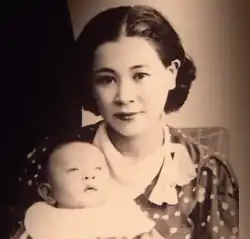 Photographie en noir et blanc d'une jeune femme avec son bébé dans les bras. La femme a des cheveux noirs et regarde la caméra.