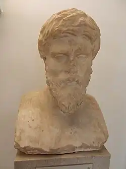 Photographie en couleurs du buste en marbre blanc d'un homme mûr et barbu.