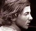 Photographie en noir et blanc d'un jeune homme aux cheveux longs, de profil.