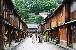 Rue dont les deux trottoirs sont surplombés par des maisons en bois à un étage.