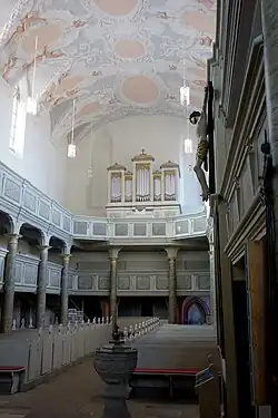 Photographie couleur d'une nef d'église, vue vers la façade et l'orgue, comportant deux tribunes qui courent des deux côtés.