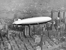 photographie vue du dessus d'un dirigeable orné d'une croix gammé, survolant une ville.