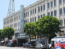 Un bâtiment blanc qui comporte beaucoup de fenêtres. Un grand panneau vertical se trouve au milieu de la façade sur lequel on peut lire Pacific. Plusieurs voitures sont arrêtées le long de la route devant le bâtiment.