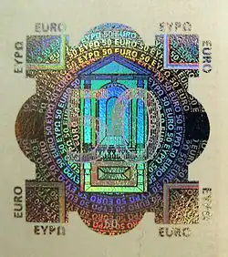 « Timbre » argenté. Au centre, le nombre 50 par-dessus une « chapelle », le tout entouré d'écritures circulaires. À chaque coin diagonal un carré ; de chaque côté un arrondi plus bombé que les cercles.