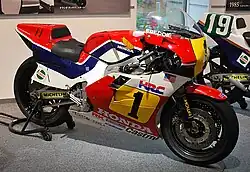 Moto de compétition Honda vue de profil, de couleur rouge, blanche, bleue et jaune.