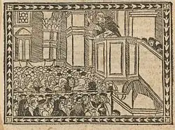Image en noir et blanc montrant un moine depuis un perchoir, en position violente, faisant le sermon à une foule dense, dans un décor architectural imposant