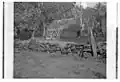 Photo en noir et blanc d'un paysage, au premier plan, un mur de pierre, au fond une maison en paille.