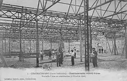Photo noir et blanc de l'usine en travaux avec de nombreux ouvriers au travail sous la charpente métallique qui n'a pas encore sa toiture